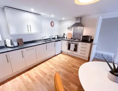 a kitchen with white cabinets and a wooden floor at Waterside apartment, central Falmouth, Vi-spring king bed, gated parking in Falmouth