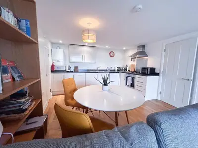 a living room with a white table and a kitchen at Waterside apartment, central Falmouth, Vi-spring king bed, gated parking in Falmouth