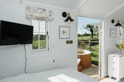 a bedroom with a flat screen tv and a window at Shepherds Hut at Chenhall Farm in Helston