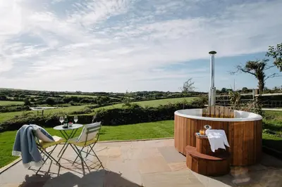 a patio with a hot tub and a table and chairs at Shepherds Hut at Chenhall Farm in Helston