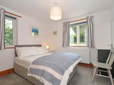 a bedroom with a bed and a chair and windows at Seaworthy in Wadebridge