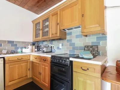 a kitchen with wooden cabinets and a black stove top oven at Court Cottage in Looe