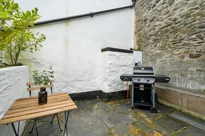 a grill and a wooden bench in a courtyard at Moll's Yard in Port Isaac