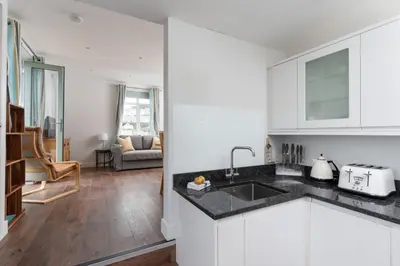 a white kitchen with a sink and a living room at 1 The Elms in St Ives