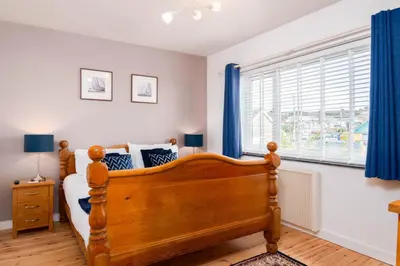 a bedroom with a bed and a window with blue curtains at The Rockpool in Praa Sands