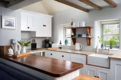 a kitchen with white cabinets and a wooden counter top at Rosewall Cottage in St Ives