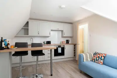 a kitchen with white cabinets and a blue couch at Skylar in St Ives