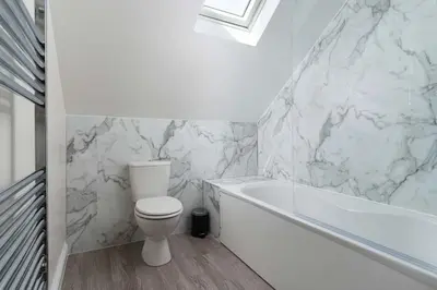 a white bathroom with a toilet and a bath tub at Skylar in St Ives