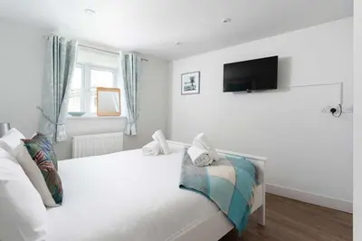 a white bedroom with a bed with a tv on the wall at 8 Sunday School Court in St Ives
