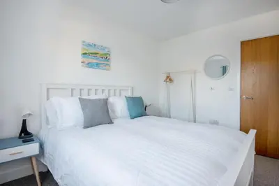 a bedroom with a white bed and a wooden door at Spacious Flat Sea Views & Private Parking Fistral in Newquay