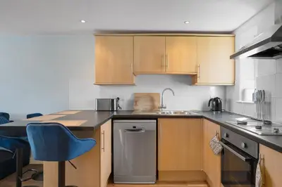 a kitchen with wooden cabinets and a blue chair at Cosy Apartment Parking Central Newquay in Newquay