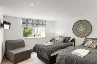 a bedroom with two beds and a chair and a window at Ranalegh Court in Saint Columb Minor