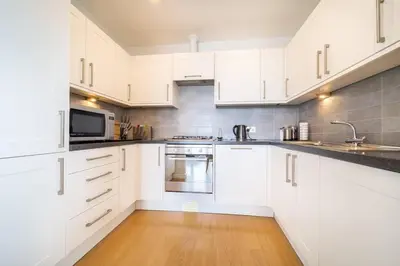a white kitchen with white cabinets and a wooden floor at Modern Apartment nr Fistral Beach Private Parking in Newquay
