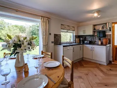 a kitchen with a wooden table with a vase of flowers at Curlew in Wadebridge
