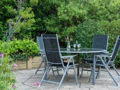 three chairs and a glass table in a garden at Curlew in Wadebridge