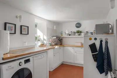 a kitchen with white cabinets and a washer and dryer at Cornish Miners Cottage St Agnes in St. Agnes
