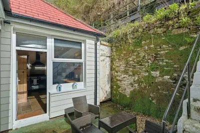 a small shed with a window next to a wall at Cosy Home on the Waterfront Private Parking in Looe
