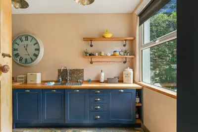 a kitchen with blue cabinets and a clock on the wall at Cosy Home on the Waterfront Private Parking in Looe