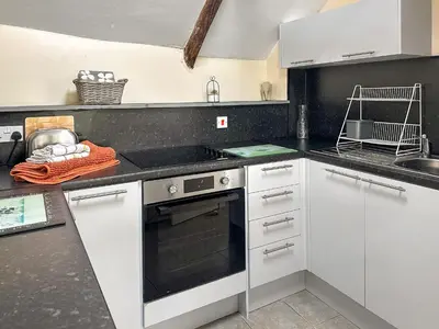 a kitchen with white cabinets and a black counter top at Pillar Box Cottage in Tintagel