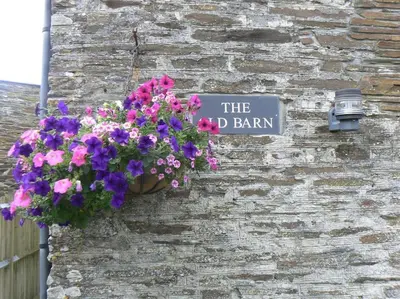 a sign on the side of a building with flowers at The Old Barn in Tintagel