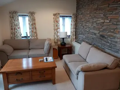 a living room with two couches and a stone wall at The Old Barn in Tintagel