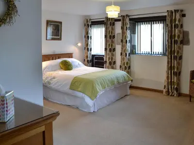 a bedroom with a bed and a desk and windows at Eglos Derry Farm Cottage - E4597 in Cury