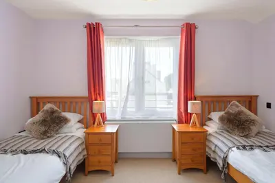 a bedroom with two beds and a window with red curtains at Townhouse Parking 1 Min Walk to Tolcarne Beach in Newquay