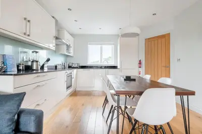 a kitchen with a wooden table and white chairs at Modern House in St Agnes Parking & Garden in St. Agnes