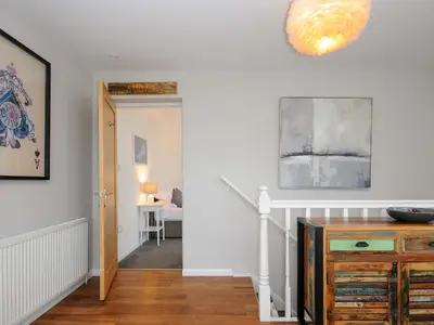 a hallway with white walls and a staircase with a wooden dresser at Waves Edge in Torpoint
