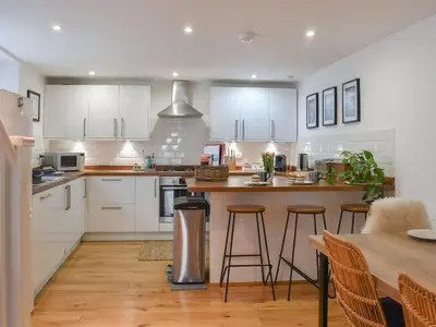 a kitchen with white cabinets and a table with stools at Stones Throw in Padstow
