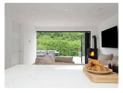 a white room with a fireplace and a table with a plate of food at Newly Refurbished Beach Lodge in Looe