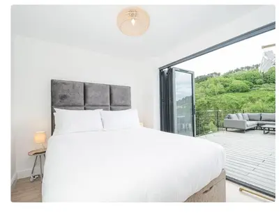 a white bedroom with a bed and a balcony at Newly Refurbished Beach Lodge in Looe