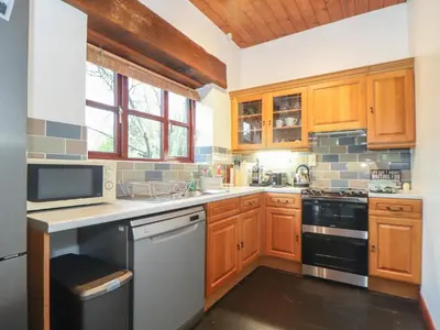 a kitchen with wooden cabinets and a stove top oven at Owl Cottage in Looe