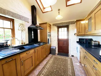 a large kitchen with wooden cabinets and a sink at Carole's Cottage - Private Parking, Sea Views, Garden & Close To Harbour & Beach in Charlestown