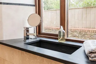 a sink in a bathroom with a mirror and a window at Hendra Barn at Hendra Barns in Newquay