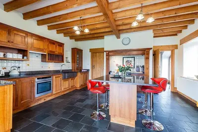 a large kitchen with wooden cabinets and red bar stools at Hendra Barn at Hendra Barns in Newquay