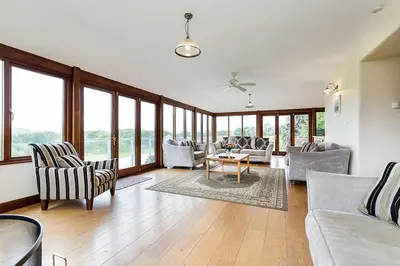 a living room with chairs and a table and windows at Hendra Barn at Hendra Barns in Newquay
