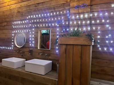a bathroom with two toilets on a wooden wall with lights at Greenfinch Lakeside Bell Tent Basic with Airbeds Only in Saint Columb Major