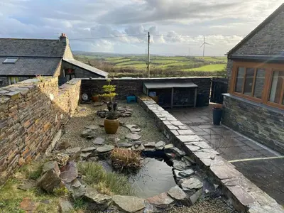 a backyard with a pond and a stone wall at Sundance Cottage Sleeps 4 in Camelford