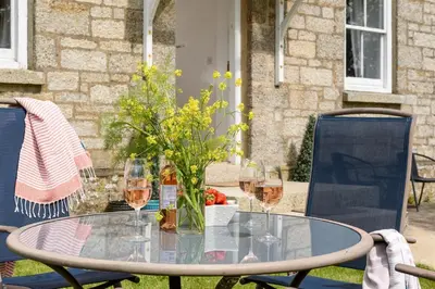 a glass table with wine glasses and flowers on it at Family Friendly Apartment above Praa Sands Beach in Praa Sands