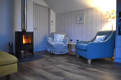 a living room with two chairs and a fireplace at Bream Barn - sea view, woodburner, easy walk to the beach, parking, full kitchen in Falmouth