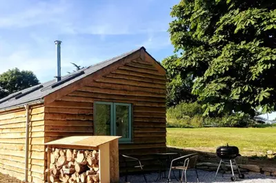 a log cabin with a grill and a table and chairs at Bream Barn - sea view, woodburner, easy walk to the beach, parking, full kitchen in Falmouth