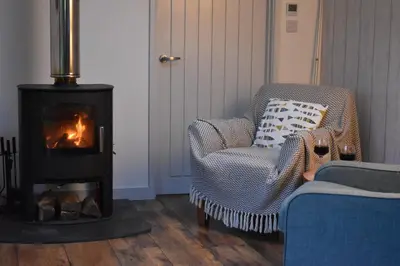 a living room with a wood stove and a chair at Bream Barn - sea view, woodburner, easy walk to the beach, parking, full kitchen in Falmouth