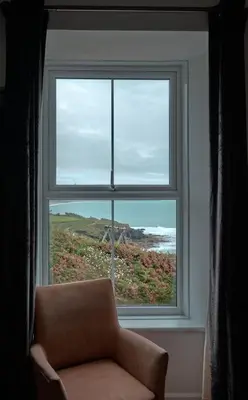 a window with a chair looking out at the ocean at Beacon Crag in Porthleven