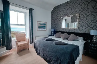 a bedroom with a bed with a mirror and a chair at Beacon Crag in Porthleven