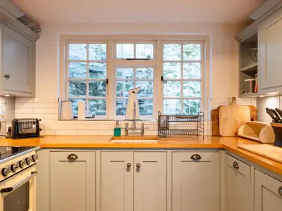 a kitchen with white cabinets and a sink and windows at Holiday Home Hillside by Interhome in Portloe