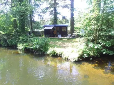 a tent in the woods next to a river at Waters Meet in Warleggan