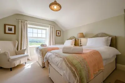 a bedroom with two beds and a chair and a window at 4 Bed in Trevillick oc-m30376 in Tintagel