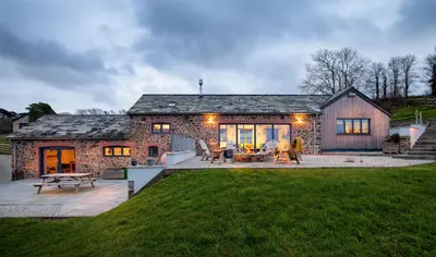 a stone house with a patio and a lawn at Songbirds in Bude