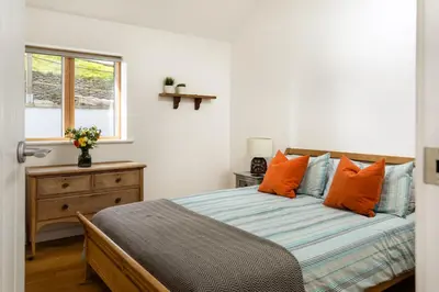 a bedroom with a bed with orange pillows and a window at Songbirds in Bude
